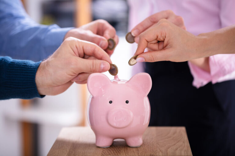 Businesspeople's,Hand,Inserting,Coins,Into,Pink,Piggybank,In,Office