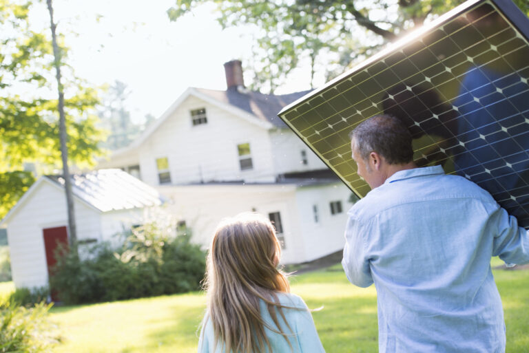 A,Man,Carrying,A,Solar,Panel,Towards,A,Building,Under