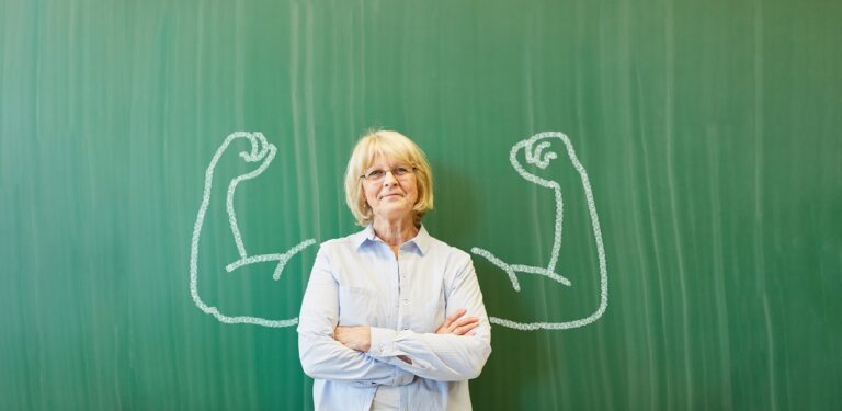 Strong,Senior,Teacher,With,Chalk,Muscles,In,Front,Of,Chalkboard