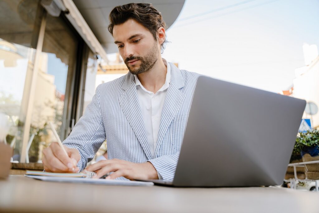 Young,Man,Wearing,Jacket,Writing,Down,Notes,While,Working,With