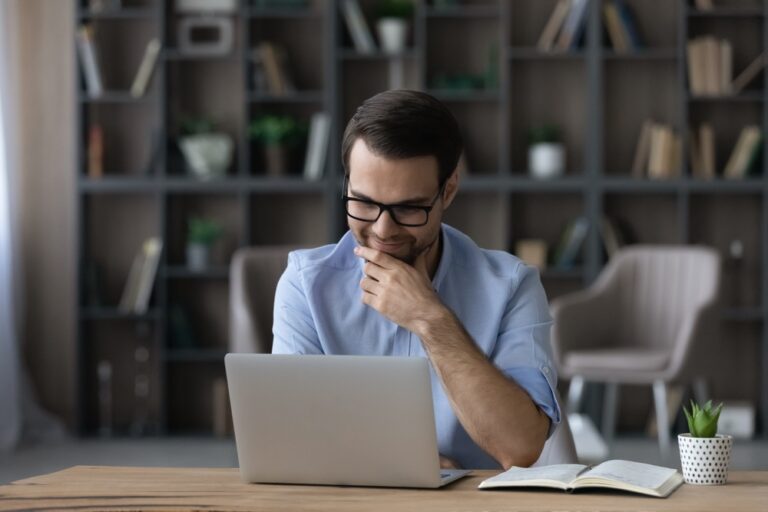 Smiling,Young,Businessman,In,Eyewear,Looking,At,Laptop,Screen,,Reading