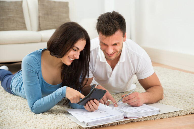 Portrait,Of,A,Happy,Young,Couple,Lying,On,Rug,Calculating