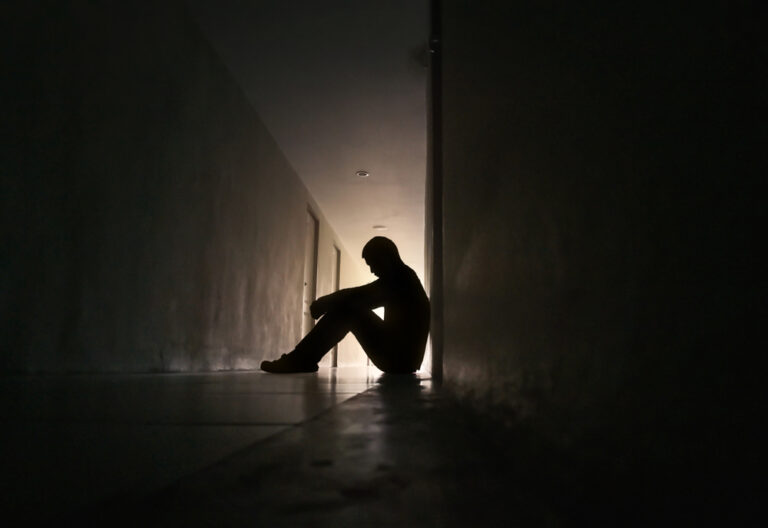 Silhouette,Of,Depressed,Man,Sitting,On,Walkway,Of,Residence,Building.