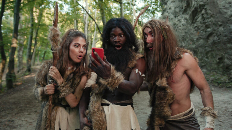 Cheerful,Group,Of,Neanderthal,Hunters,Using,Modern,Technology,Smartphone,Cheering