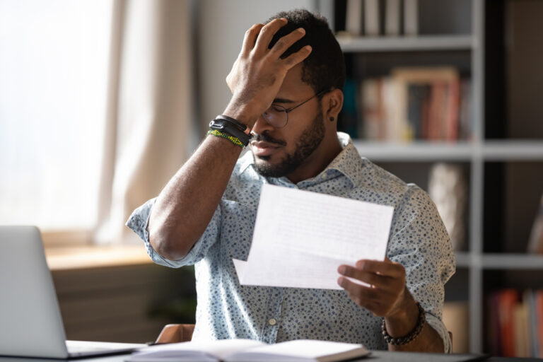 Stressed,African,Businessman,Sit,At,Desk,Hold,Paper,Letter,Reading